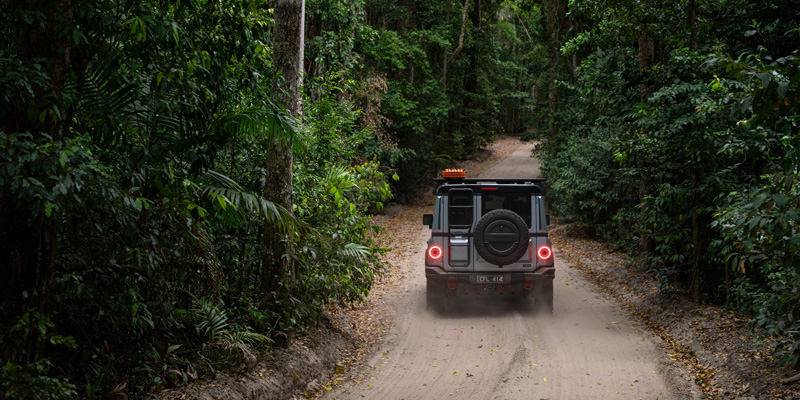 Ineos Grenadier driving on the road through a forest