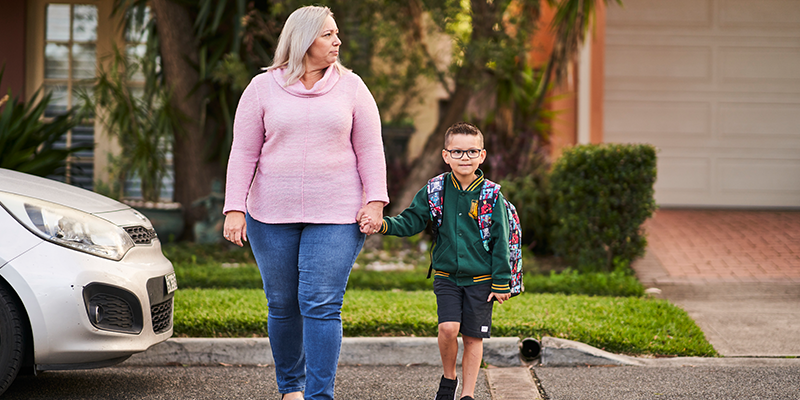 A woman crossing the road holding hands with a small boy in school uniform