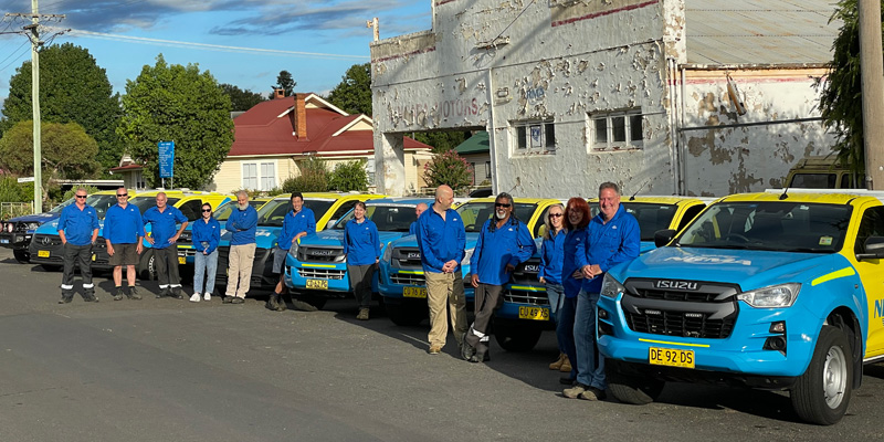 a group of volunteers standing next to blue and yellow nrma vehicles