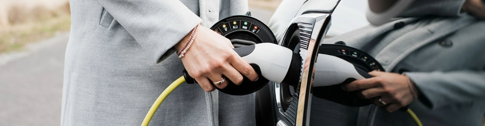 A lady wearing a grey coat, charging her electric vehicle.