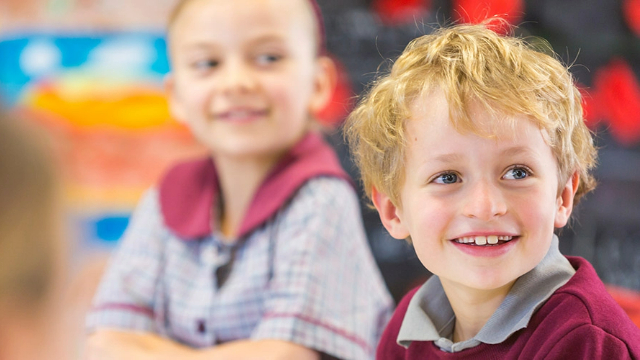 primary-school-kids-in-class-640x360 A boy and girl sitting in a classroom, turned towards the camera and smiling.