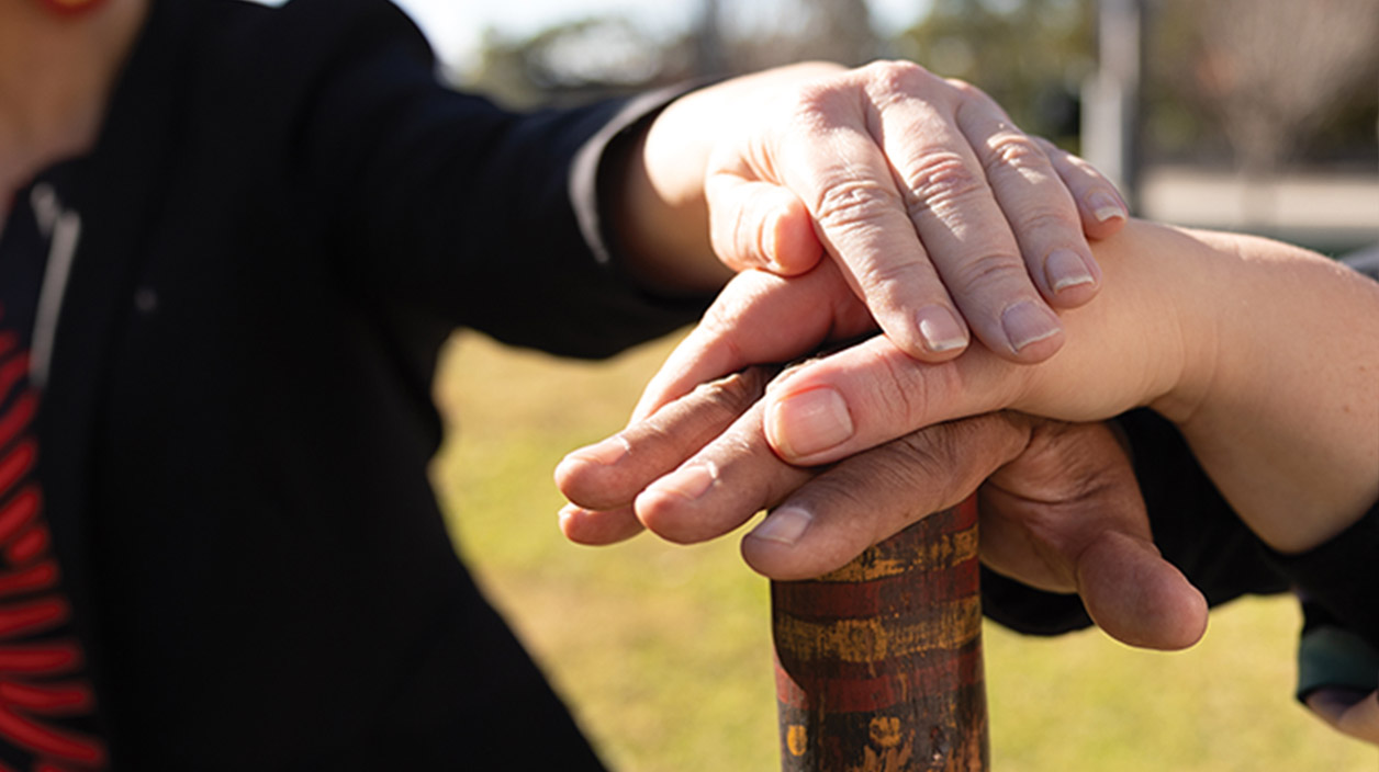 Hands stacked on a wooden stick with Aboriginal markings
