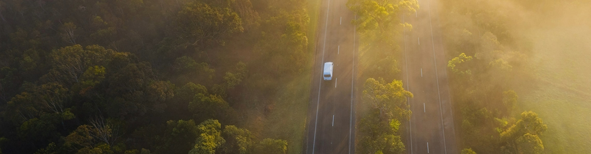 sunny-forested-road-1920x500 Aerial view of a four lane highway separated by trees on a hazy, sunny day.