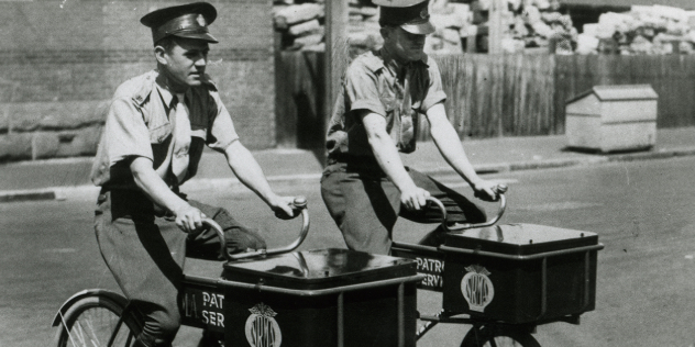 black and white image of two nrma road patrol employees using bicycles in the CBD to save on petrol during 1940s rationing