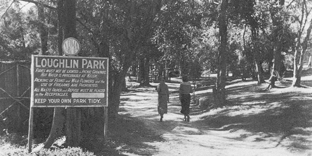 black and white photo from the 1930s of a sign to NRMA's Loughlin motor park and two women walking into the park road