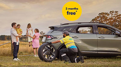 NRMA Roadside assistance staff member helping to replace tyre for vehicle on the side of the road while family of four look on