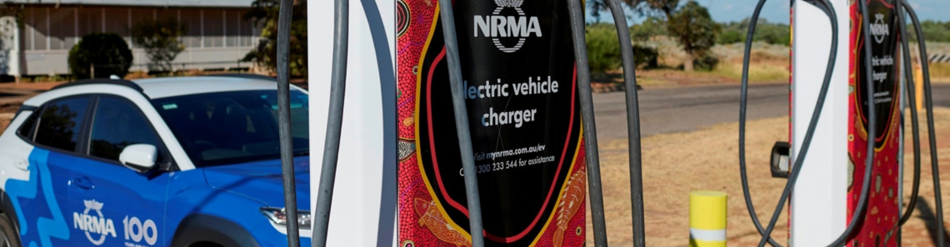nrma-remote-charging-station-1920x500 Two EV charging stations, decorated with Aboriginal art dot designs, along a sunny, rural road.
