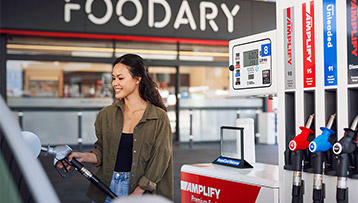 A woman is filling her car with fuel at an Ampol fuel station, focused on the pump as she prepares to refuel
