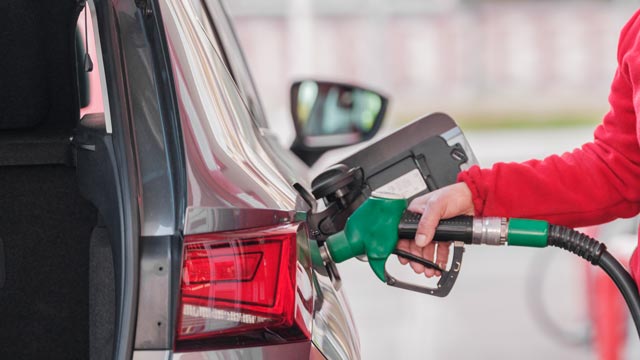 Arm in red sleeve putting fuel in a car seen from rear of car