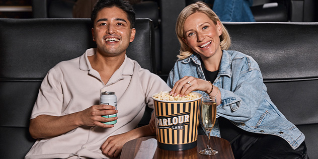 A man and a woman share a bucket of popcorn in gold class