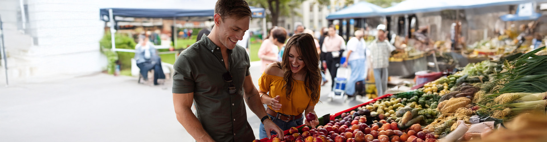 A man and a woman looking at produce at an outdoor market