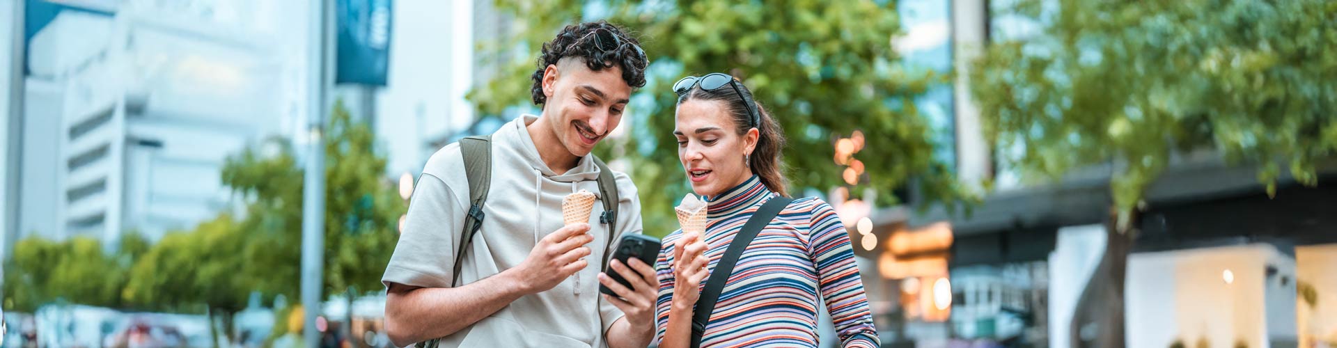 A couple eating icecream is a leaefy street looking at a phone