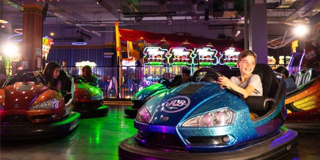 happy child drives a blue dodgem car with fairground rides in the background