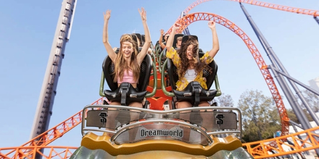 two happy teen girls with their arms raised at the front of a dreamworld roller coaster about to descend