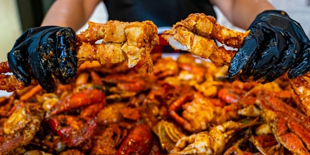 black rubber-gloved hands of person dining on a pile of orange crab claws