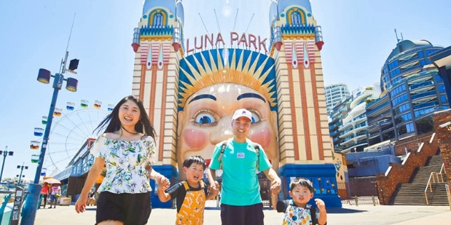 happy family of man, woman and two small boys smiling as they exit Luna Park with the iconic clown face gate in the background 