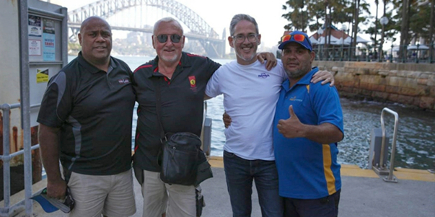 Four men standing together, side-by-side with the Sydney Harbour Bridge in the background.