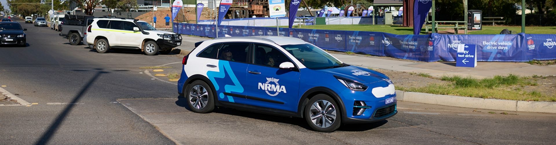 A blue and white NRMA branded vehicle travelling on a suburban road and taking a bend.