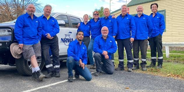 A group of volunteers dressed in blue, huddled together looking at the camera and smiling.