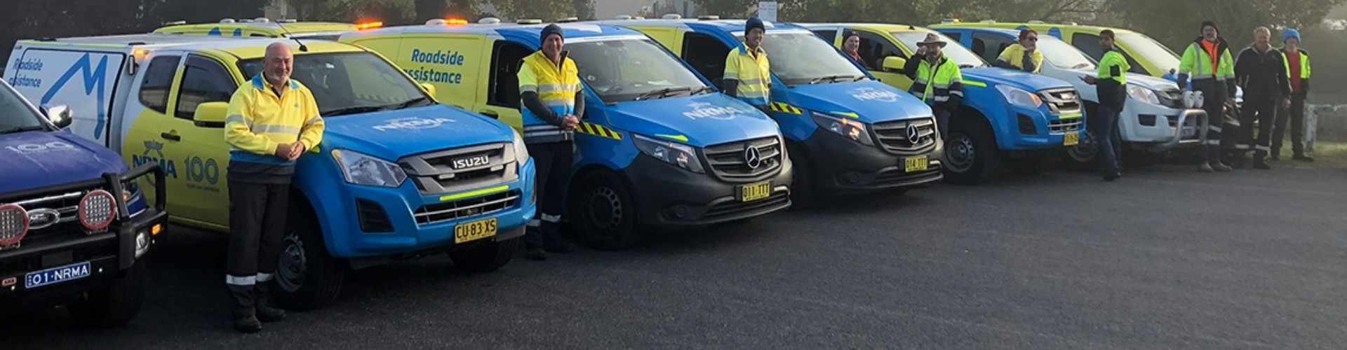 A row of NRMA vehicles lined up side by side, with one volunteer standing toward the front of each vehicle.