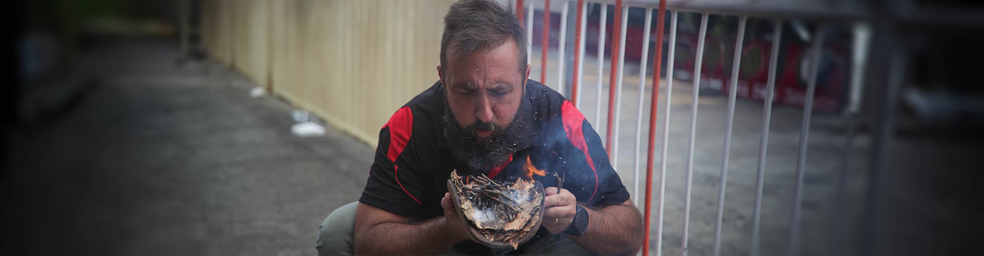 Indigenous man blows on bundle of leaves and sticks as part of smoking ceremeny