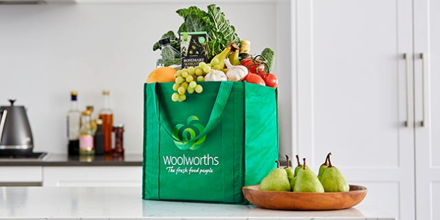 green Woolworths shopping bag full of fresh fruit and vegetables on a kitchen bench top