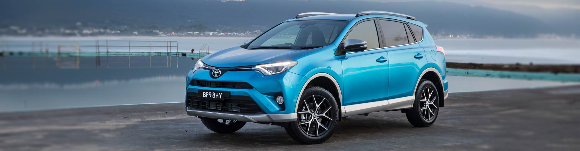 A blue 2016 Toyota Rav4 GX AWD parked in front of an ocean pool