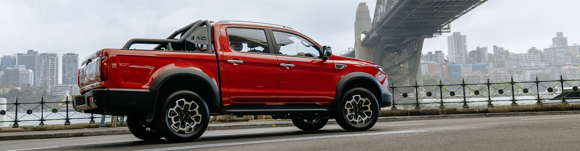 Red ute drives in front of Harbour Bridge on smoggy day