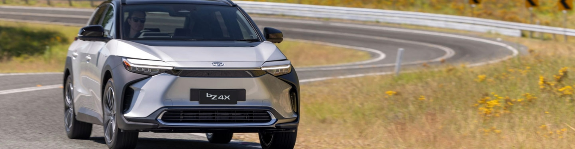 Front view of a silver, 2024 Toyota BZ4x driving along a road.