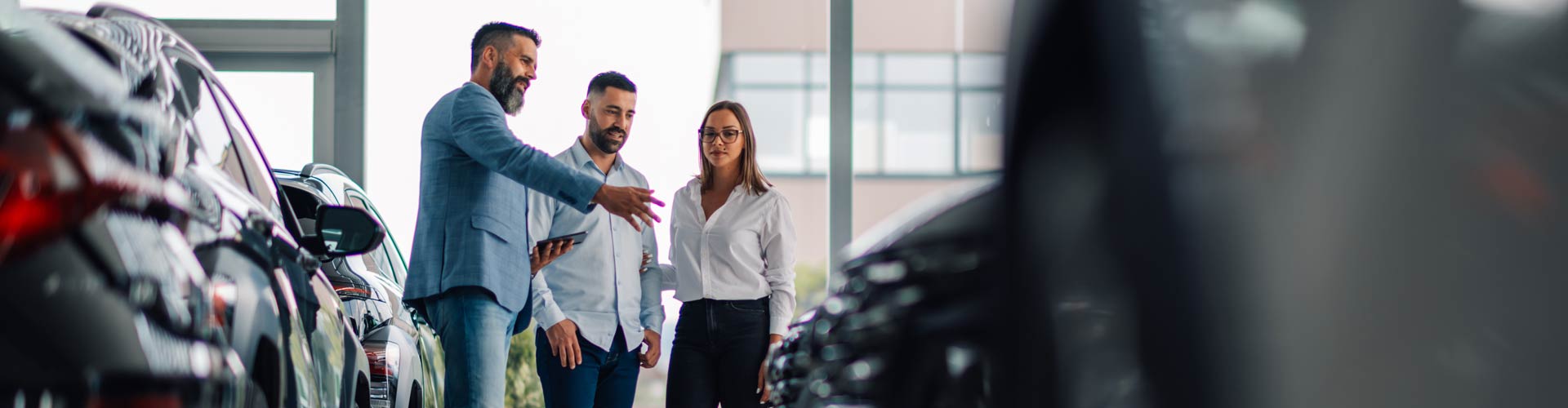 A couple stands with a salesperson in a new car showroom
