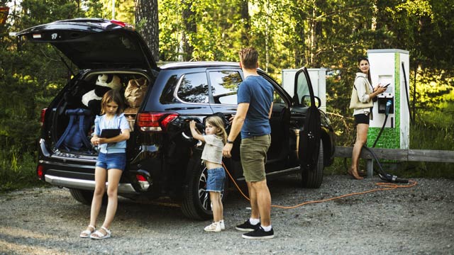 A family stands by their EV charging it in a bush setting