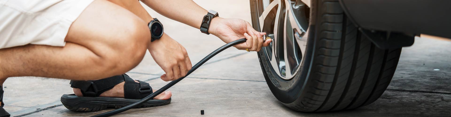 A man kneels to put air in the tyre of a car