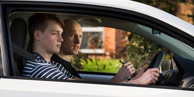 Young man sits in driver seats learning to drive next to teacher