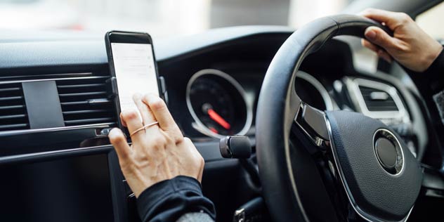 A hand touches a mobile phone on a car dashboard