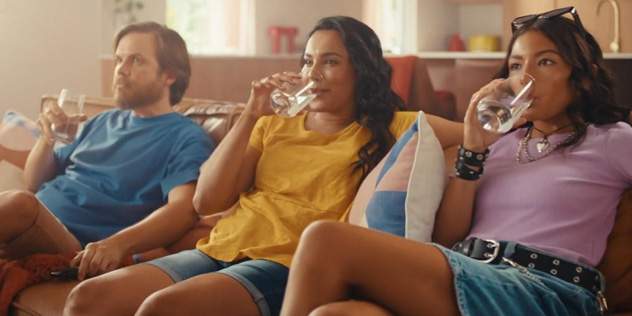 Three young adults sit on a couch drinking water from glasses