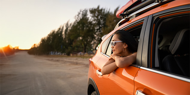 A woman looking out the rear window of orange car with her elbows out