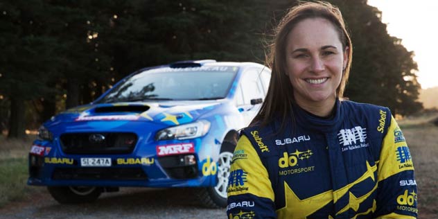 Molly Taylor standing in blue and yellow jacket in front of blue Subaru
