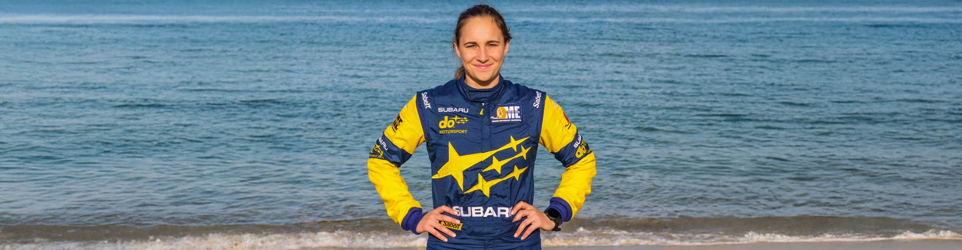 Rally champion Molly Taylor in a blue and yellow jacket in front of the ocean
