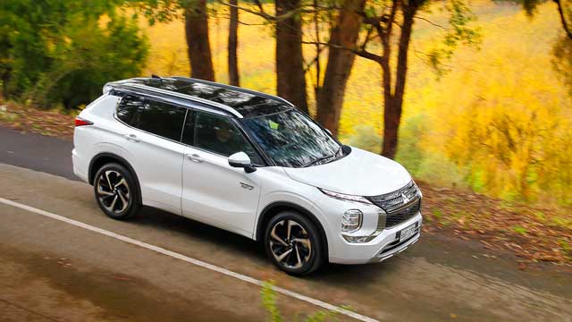 A white 2022 Mitsubishi Outlander Plug-In Hybrid Electric Vehicle driving on a country road