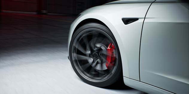 Blurred front wheel of a white Tesla Model 3 Performance with red brake caliper