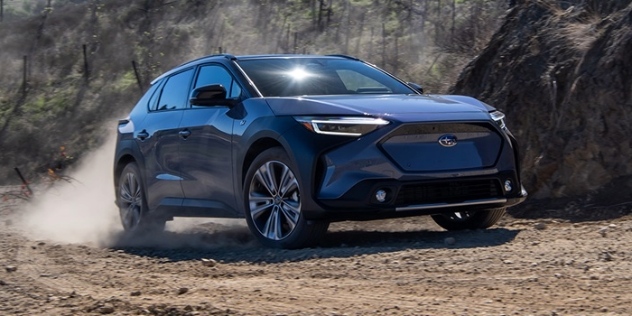 A 2023 Subaru Solterra kicks up dust as it drives across a rocky landscape 