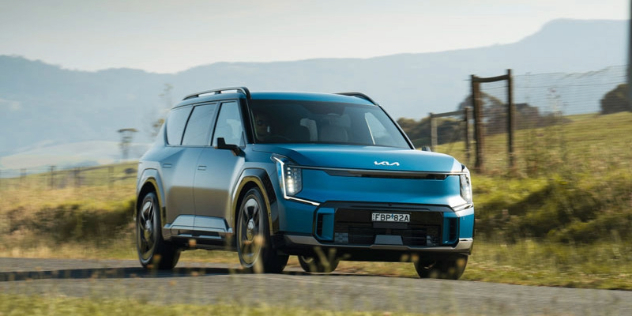 A blue 2024 Kia EV5 drives along a country road