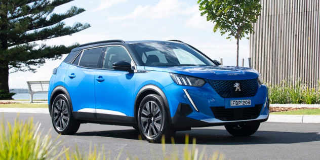 A blue 2024 Peugeot e2008 drives through a seaside town 