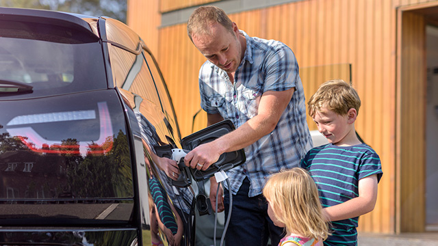 Children stand by watching as an adult plugs in their EV 