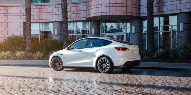 Side view of a white Tesla parked in front of a building.