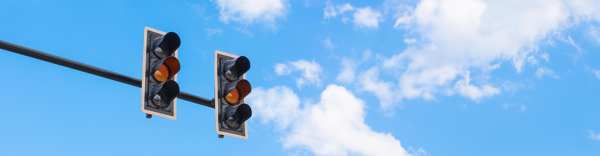 Traffic lights on orange against blue and cloudy sky
