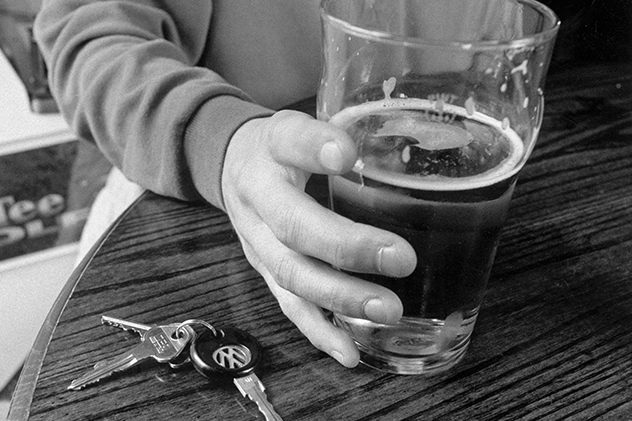 Person holding an alcoholic drink on a table next to car keys