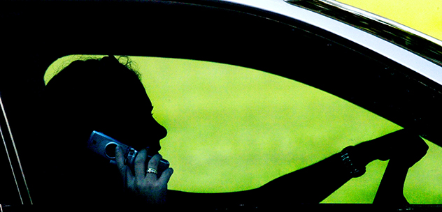 Woman in a car holding a phone in one hand with the other on the steering wheel