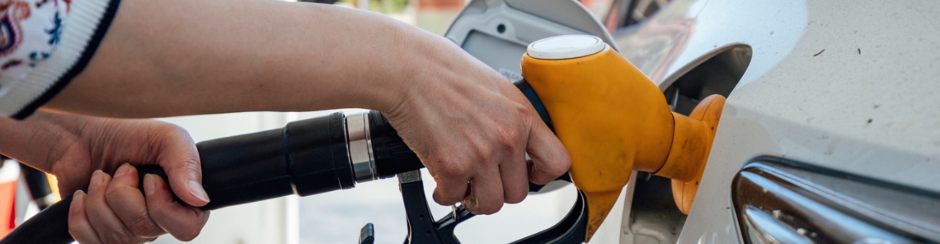 Filling up at the bowser close up of woman's hand putting yellow fuel nozzle into her car
