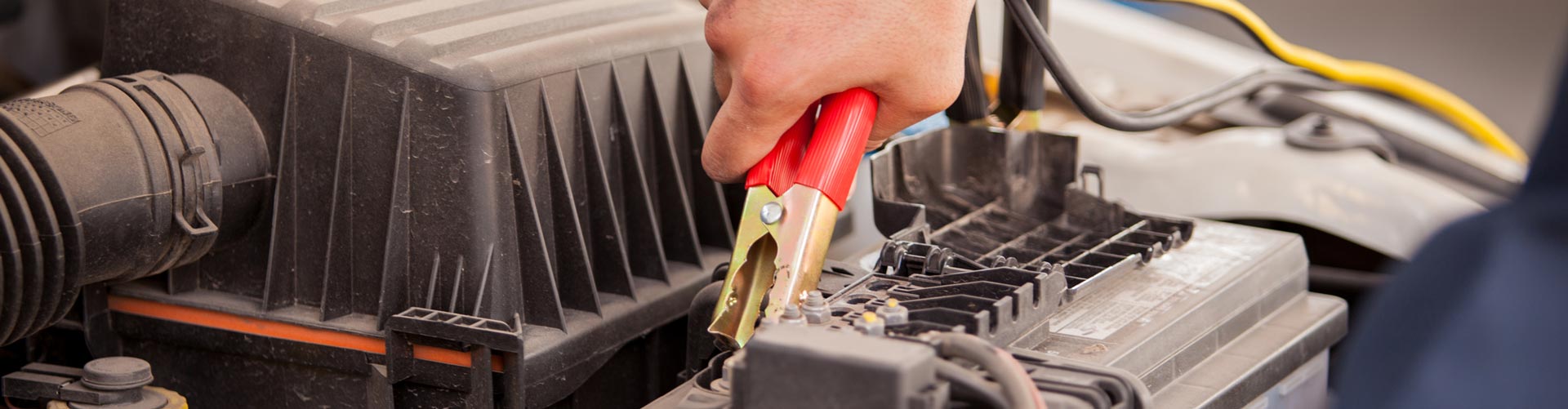 A hand puts a jumper lead on a car battery